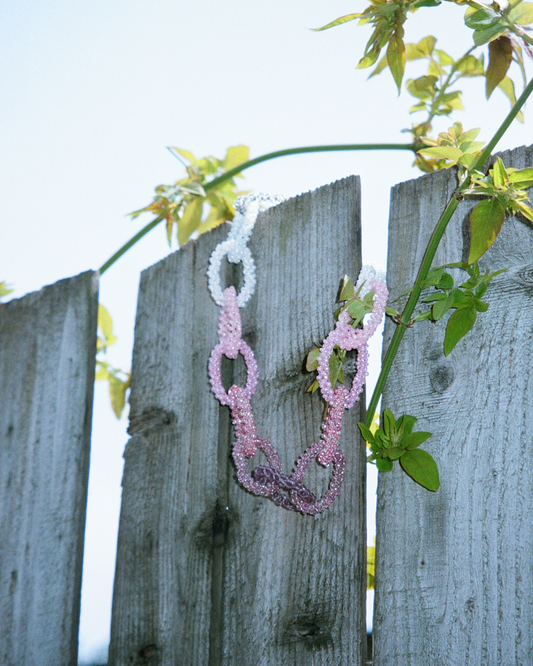 Pink beaded necklace on a wooden fence with green leaves