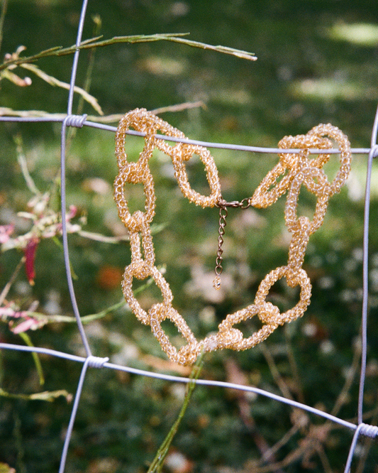 Gold chain necklace hanging on a wire fence with a blurred natural background