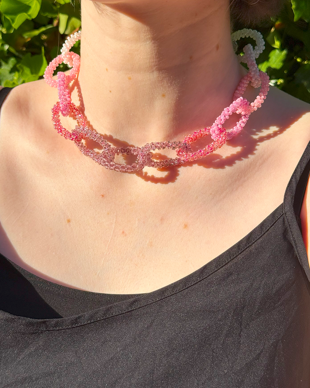 Person wearing a pink beaded necklace with a blurred green background
