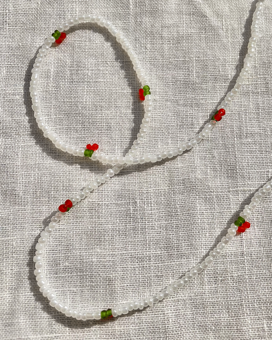 Beaded necklace with red and green accents on a textured fabric background