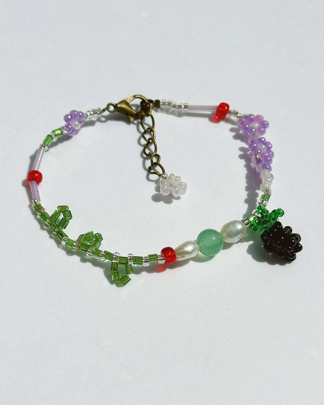 Beaded bracelet featuring jade bead, freshwater pearls, and blackberry charm on white background.