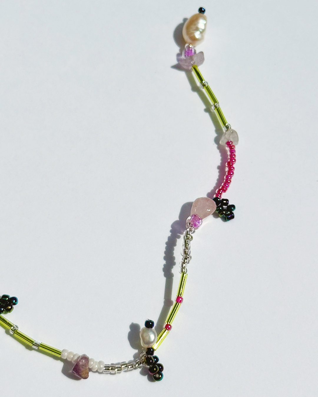 Part of a colourful beaded bracelet on a white background with pearls and pink quartz