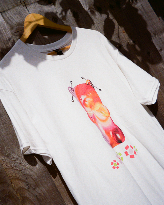 White t-shirt featuring a large 3D art print of a translucent red gummy bear with metal piercings and geometric flowers.
