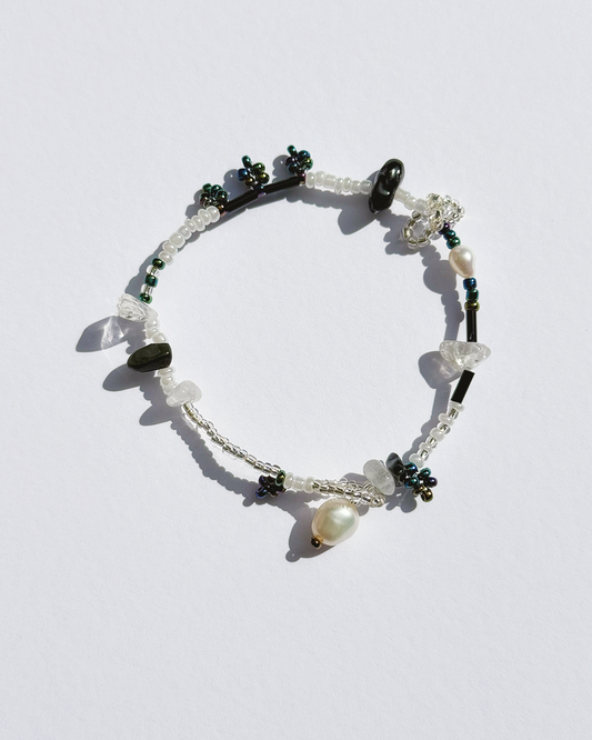 A delicate beaded bracelet with white translucent crystal beads, dark green faceted beads, a white pearl, and a silver-toned toggle clasp, displayed on a light white background.