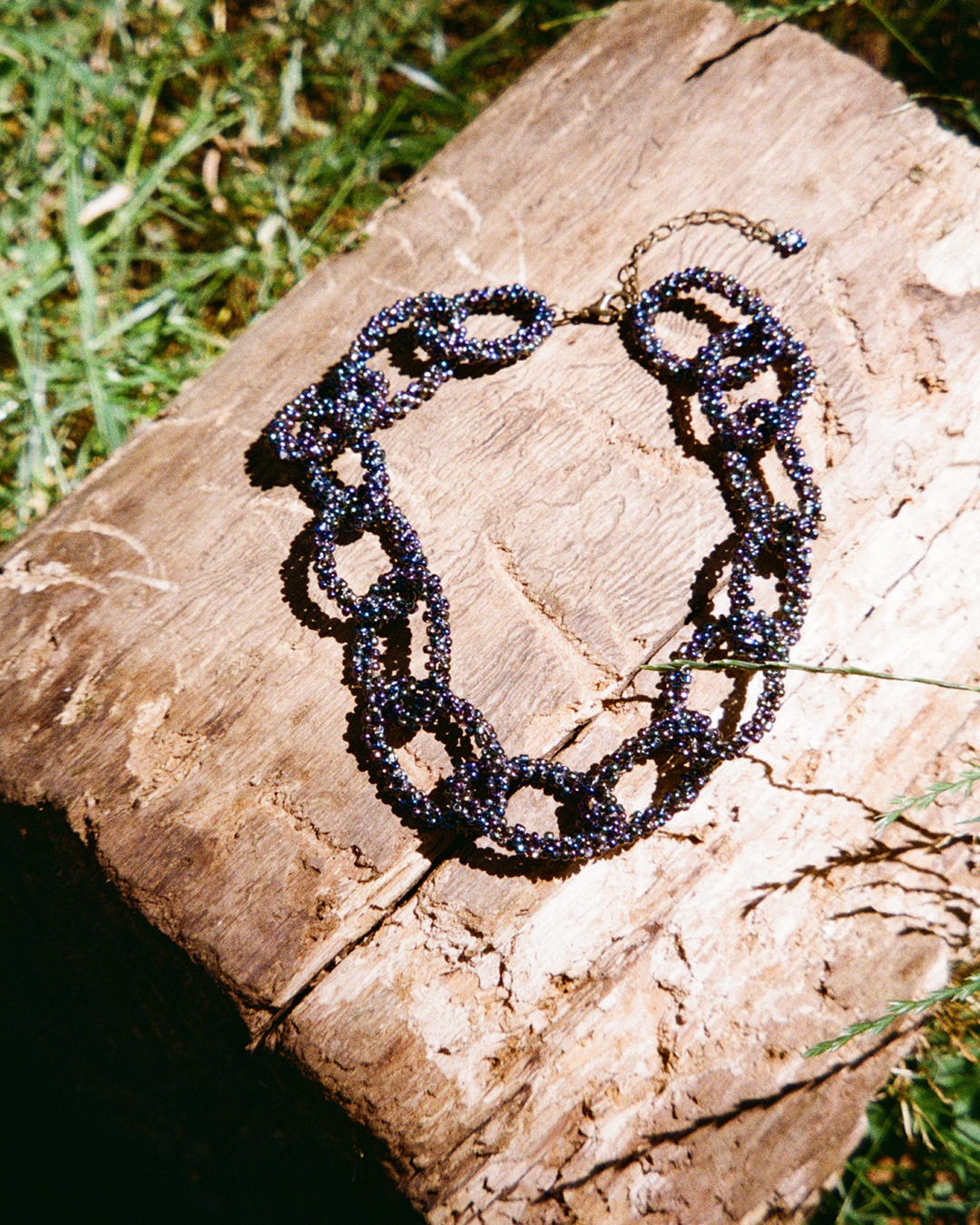 Necklace with black rainbow beads on a wooden log outdoors