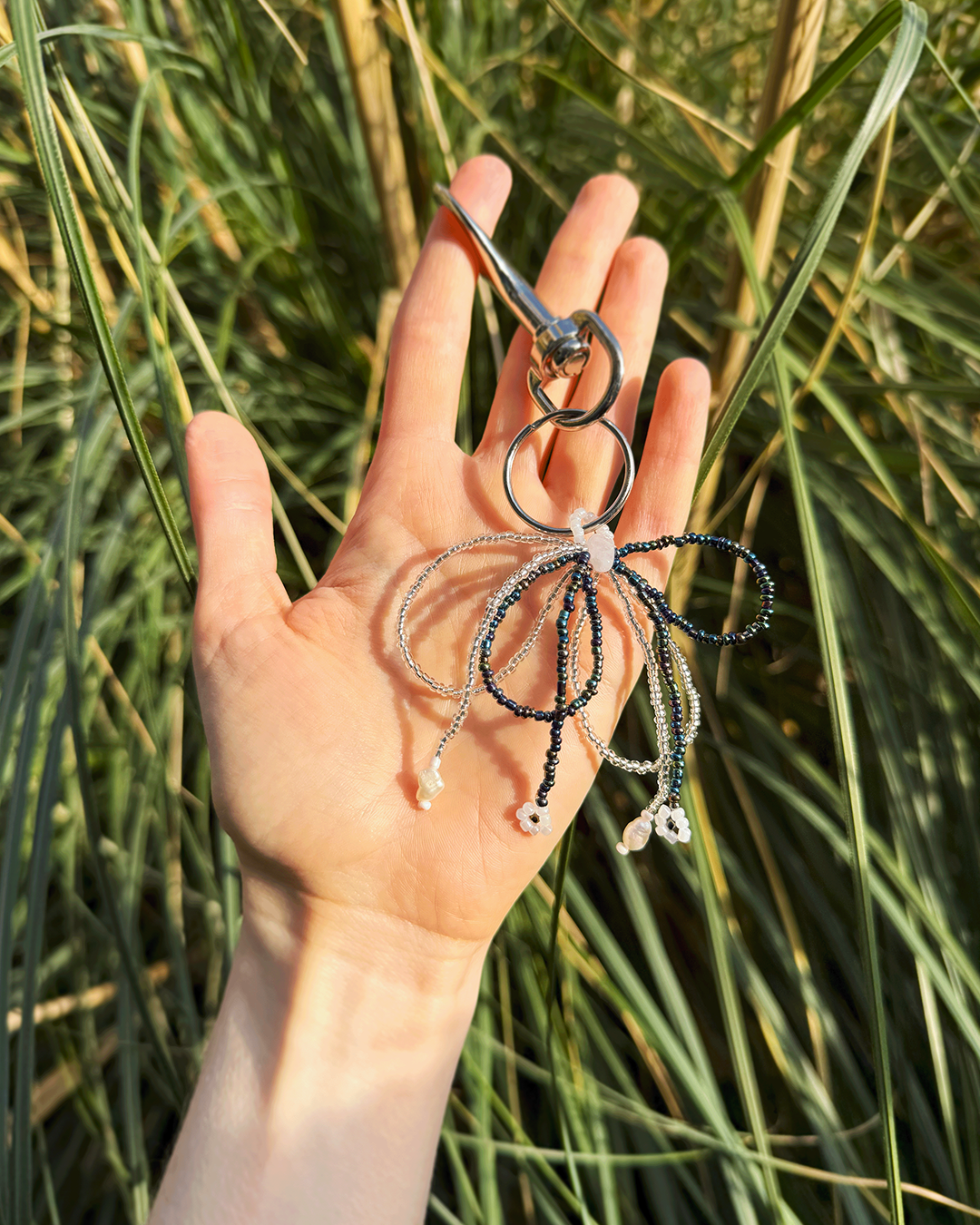 Hand holding a beaded keychain with grass in the background