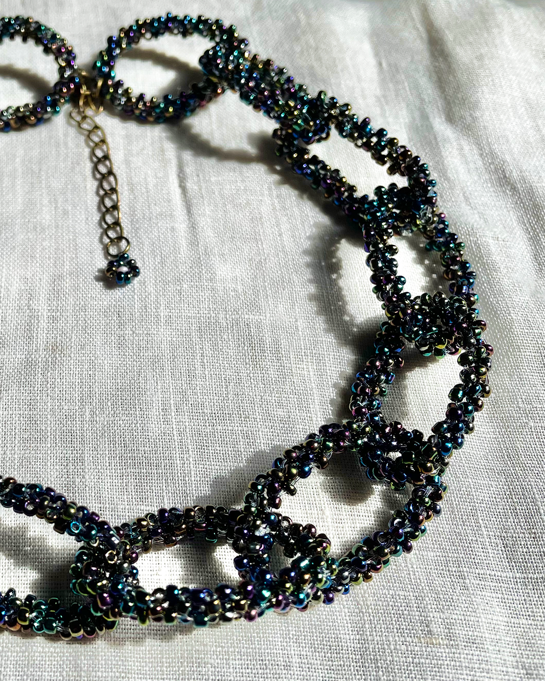 Black Rainbow beaded necklace on a textured white fabric background