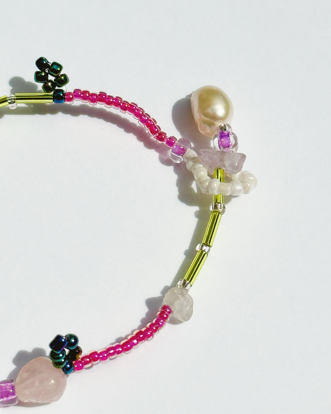 Beaded bracelet with pink, green, and silver beads with pearls and crystals on a white background