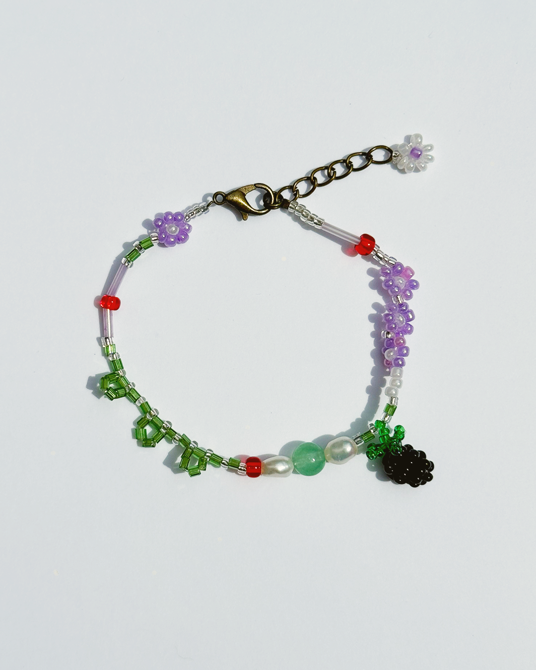 Beaded bracelet featuring jade bead, freshwater pearls, and blackberry charm on white background.