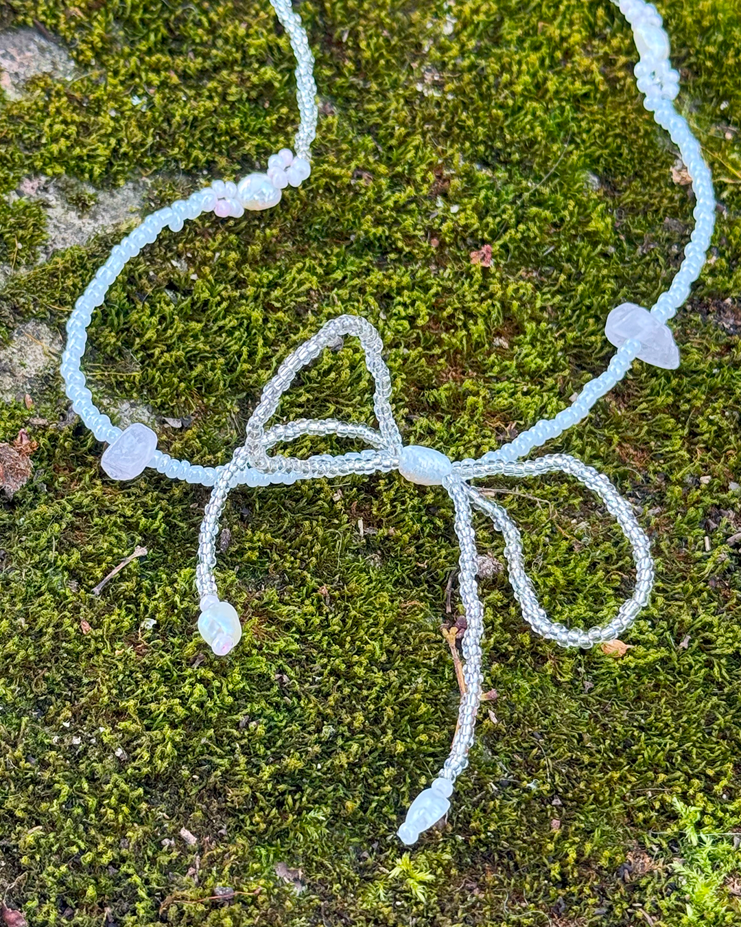A bow necklace with small beads on a green moss background