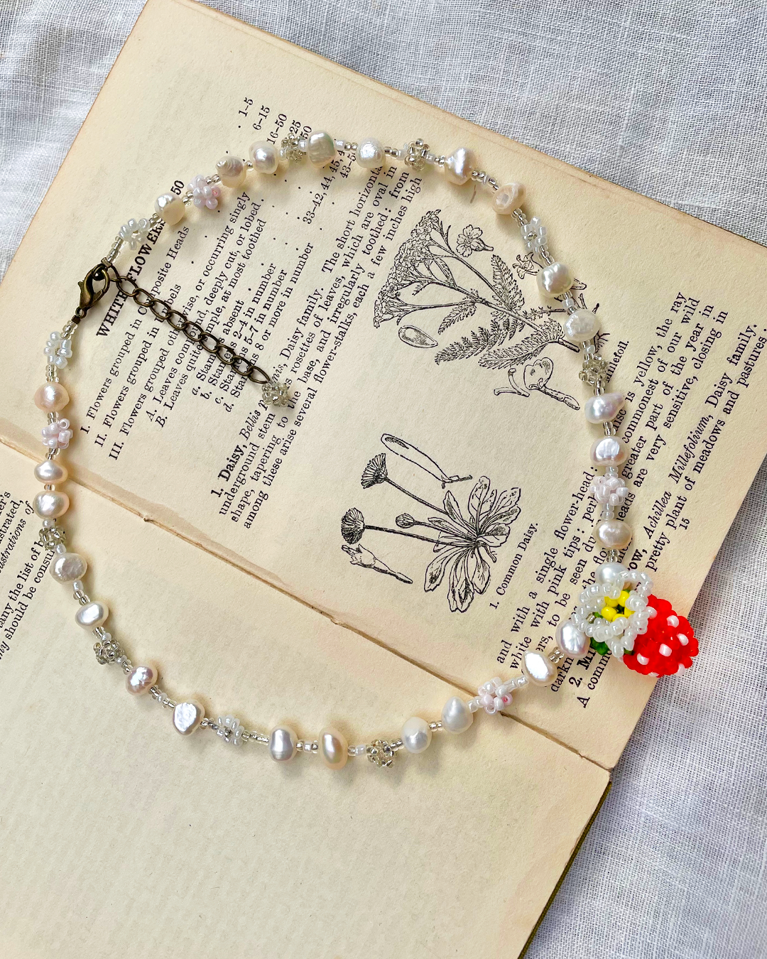 Pearl necklace with a red and white berry pendant on an open book