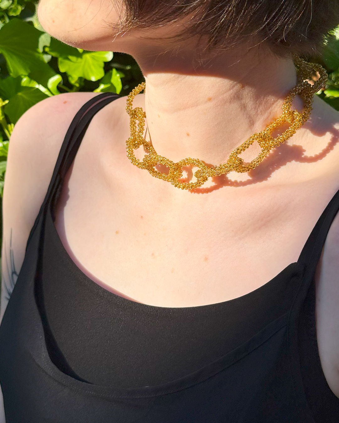 Person wearing a gold necklace with a green outdoor background