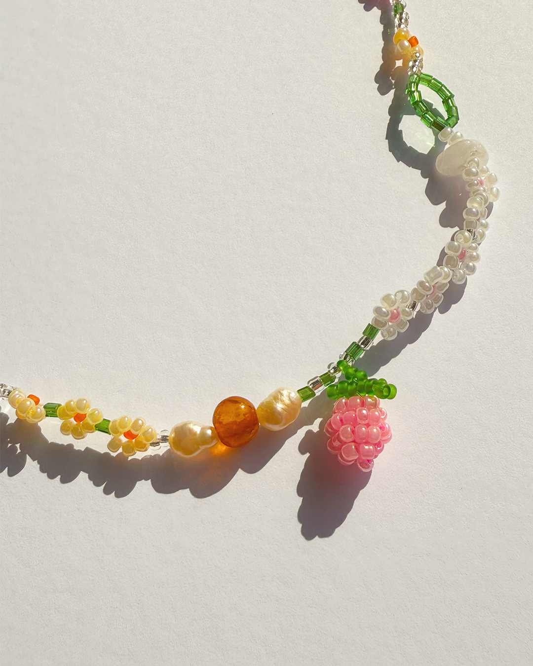 Colorful beaded necklace with floral and berry charms on a light background