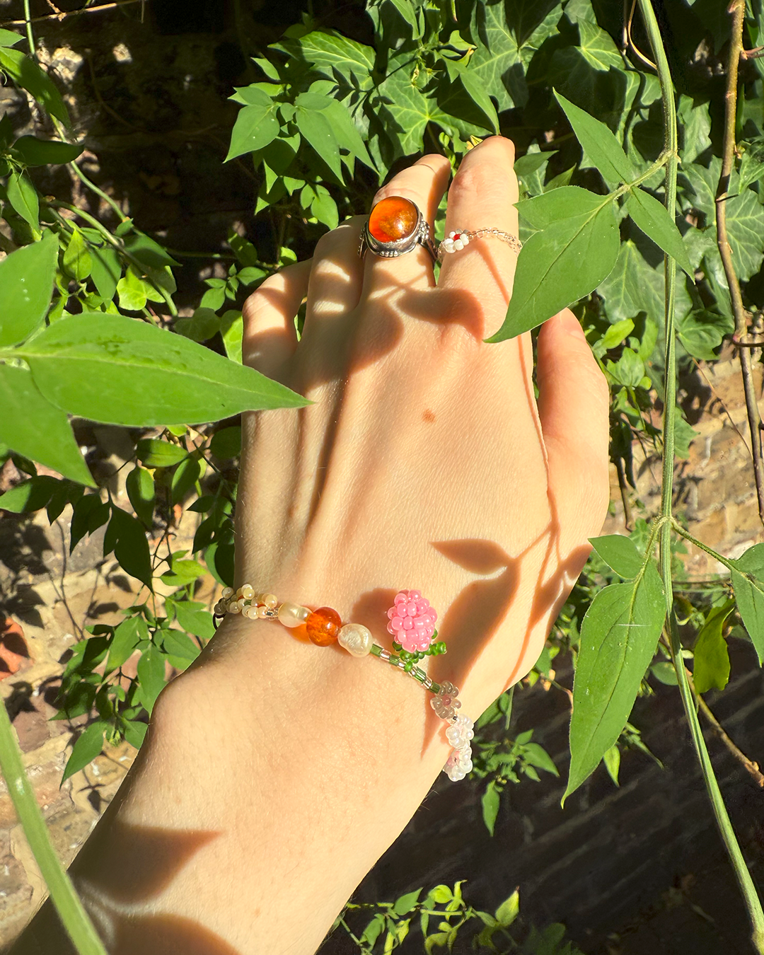 Hand wearing a bracelet with a ring, set against a natural background of leaves and plants.