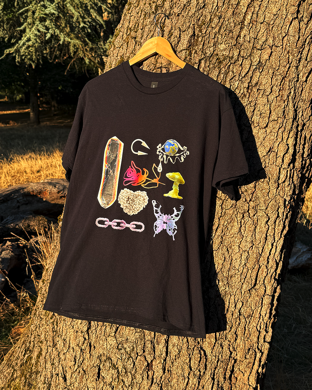 Black t-shirt featuring surreal 3D art: liquid butterfly, chrome chain, and glowing mushroom objects hanging on a tree.