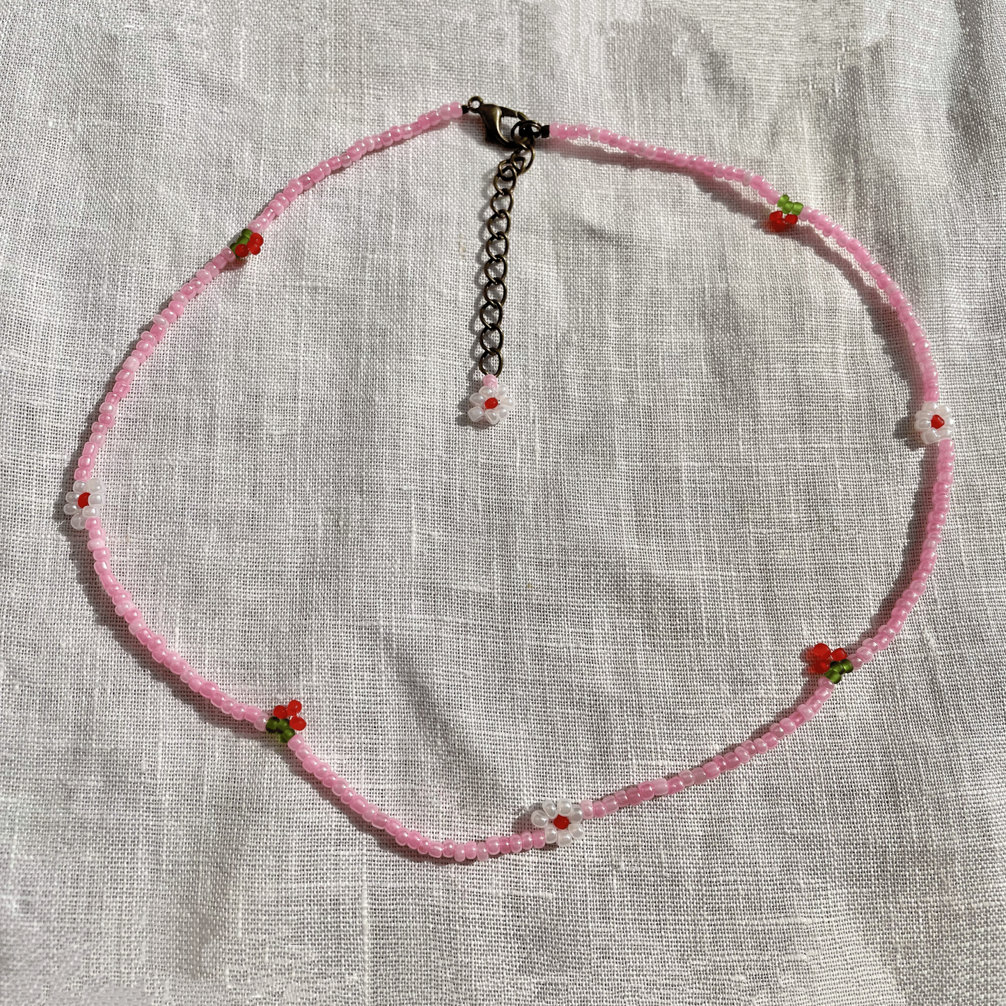 Pink beaded necklace with small red flowers on a light fabric background