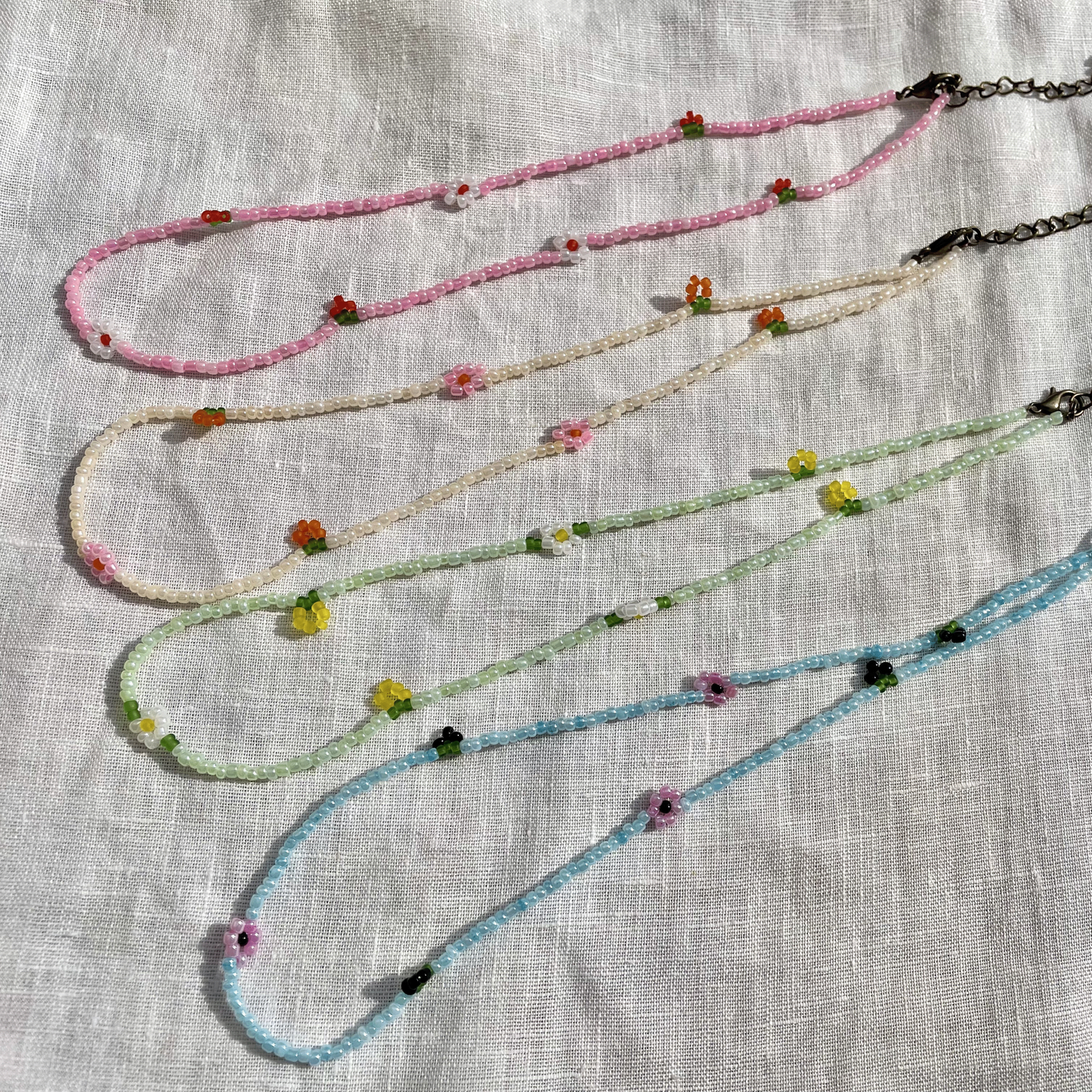 Four beaded necklaces with floral beads on a textured fabric background