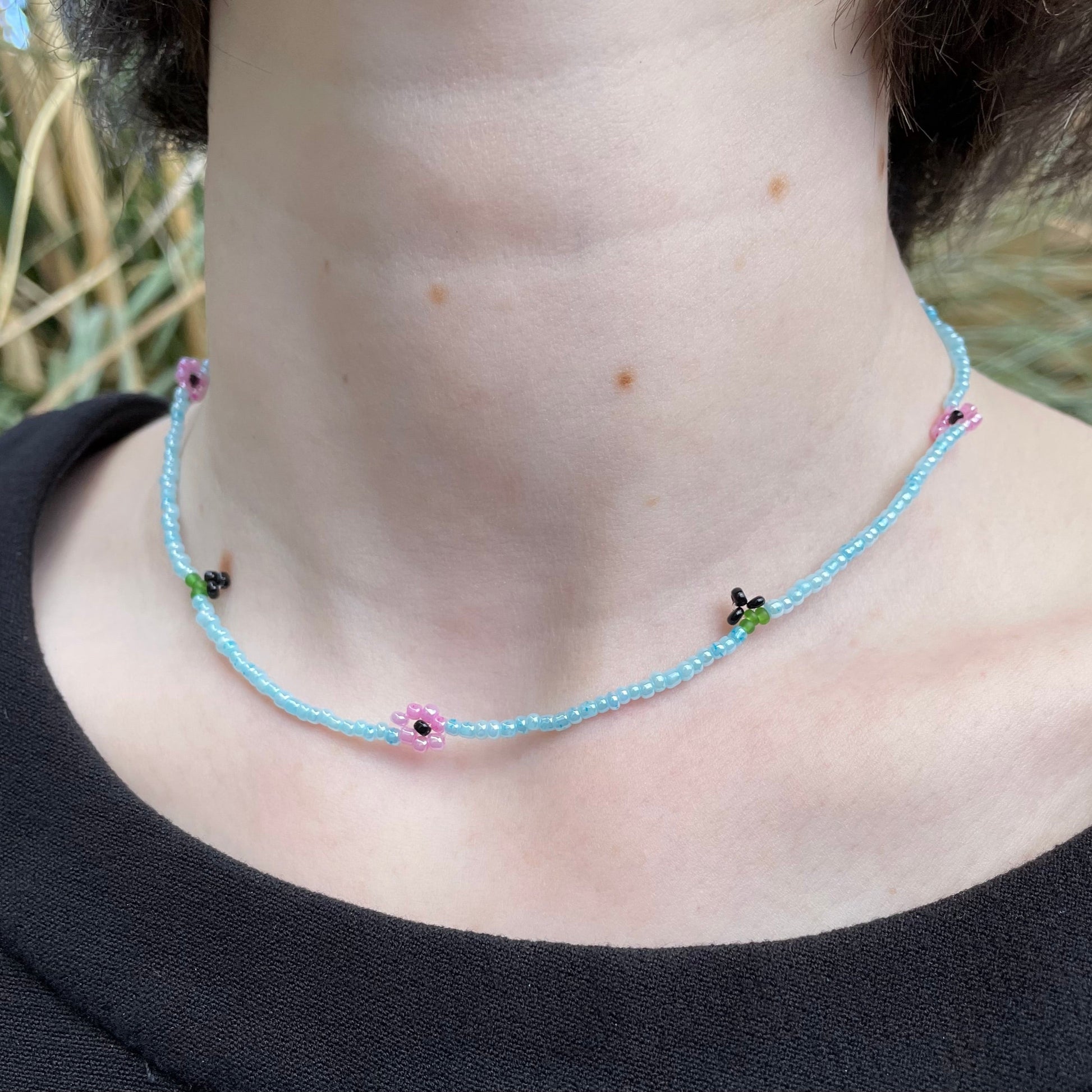 Necklace with small flowers worn by a person against a natural background